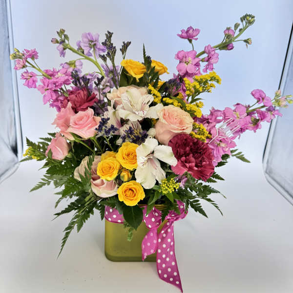 Colorful mixed flower arrangement in a green cube vase with a pink polka dot ribbon.
