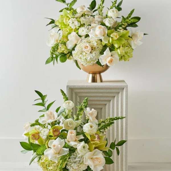Two white and green floral arrangements in gold pedestal vases
