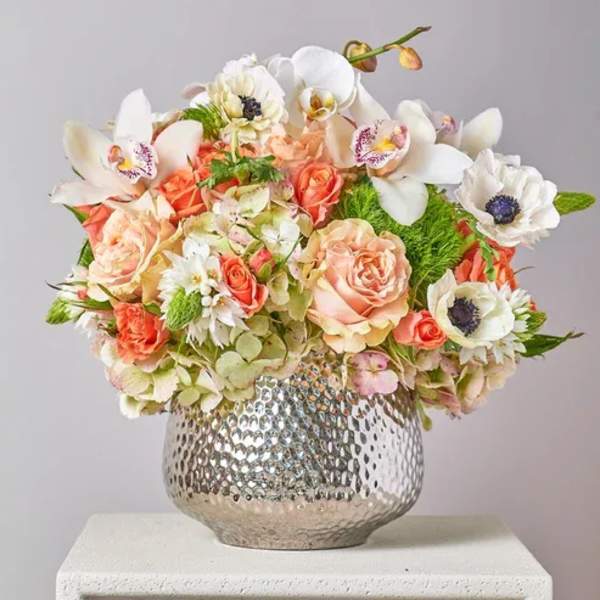 Mixed bouquet of peach and white flowers in a silver vase