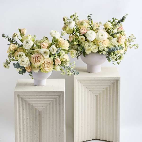 Two pastel floral arrangements in white pedestal vases