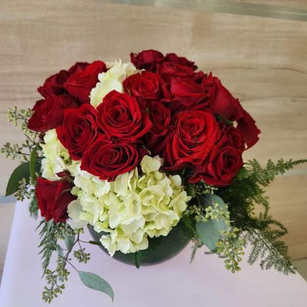 Low round arrangement of red roses and white hydrangeas in a green glass vase