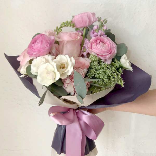 Hand-tied bouquet of pink and white flowers wrapped in dark paper with a satin ribbon.