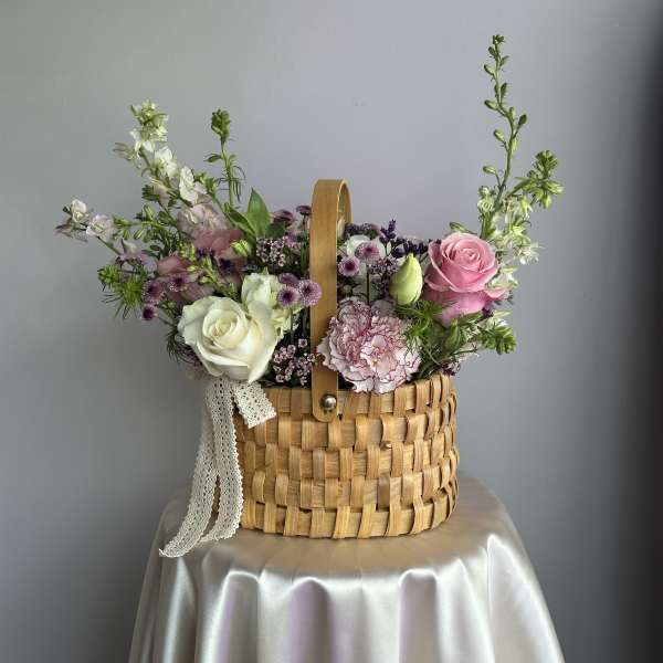 Pastel pink and white flower arrangement in a woven basket on a draped table.