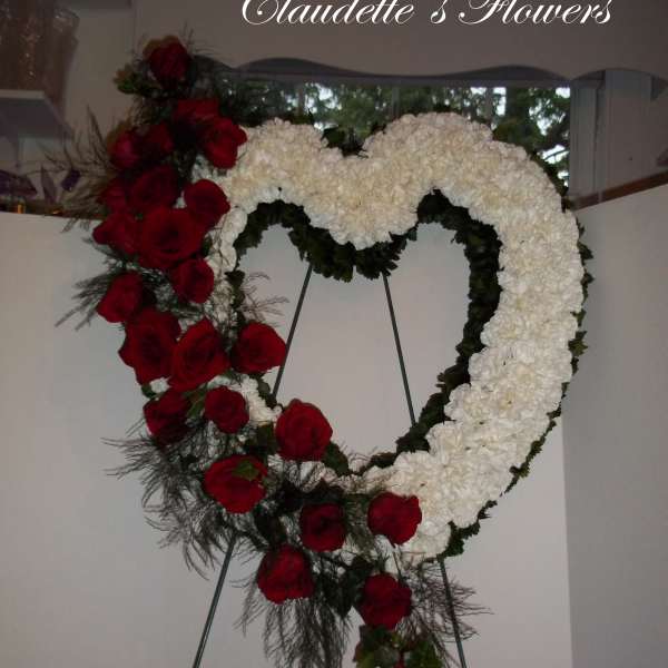Heart-shaped floral wreath with red roses and white flowers on an easel