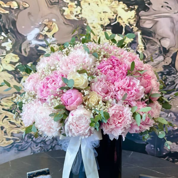 Pink peony and rose bouquet in a black vase with white ribbon