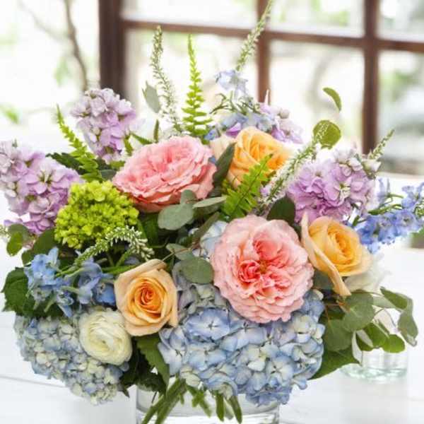Pastel bouquet of roses, hydrangeas, and purple blooms in a glass vase
