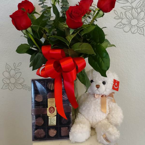 Red roses in a glass vase with a teddy bear and chocolate box