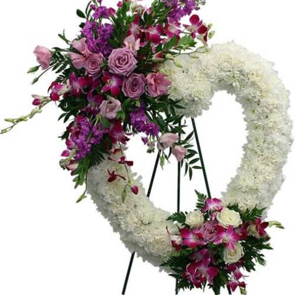 Heart-shaped white sympathy wreath with purple and pink flowers on a standing easel