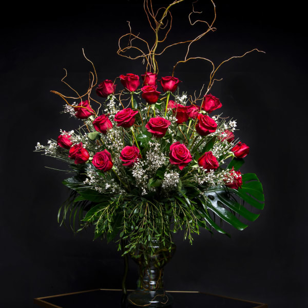 Tall bouquet of red roses in a glass vase with curly branches