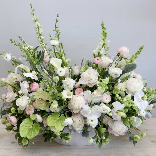 Low, wide arrangement of white and blush flowers with orchids and calla lilies in a white bowl