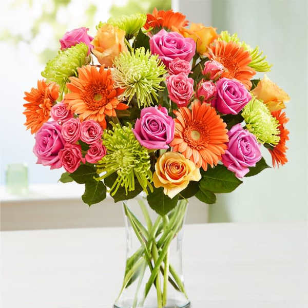 Mixed pink, orange, and green flowers arranged in a clear glass vase
