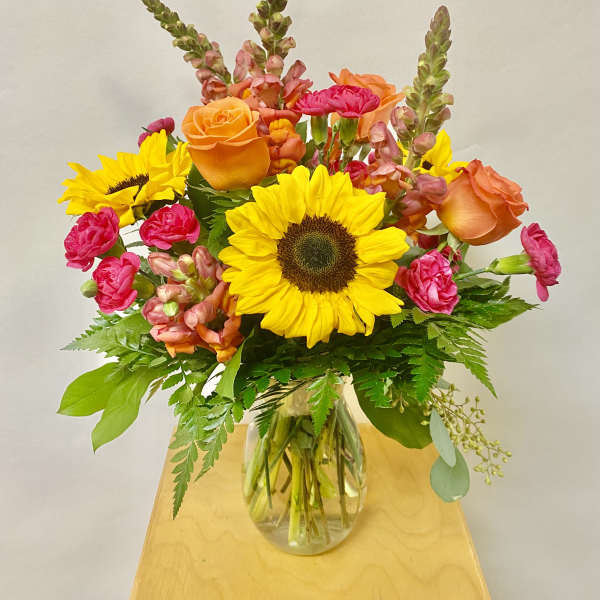 Bright mixed bouquet with sunflowers, orange roses, and pink blooms in a glass vase