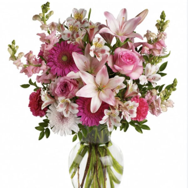 Pink and white lilies, roses, gerbera daisies, and other blooms arranged in a clear glass vase