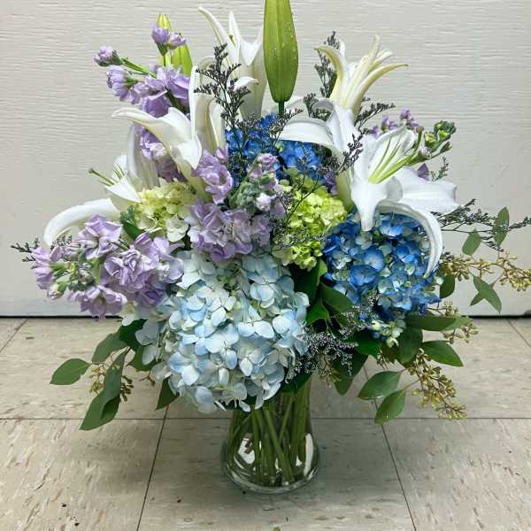 Blue and lavender hydrangea arrangement with white lilies in a glass vase