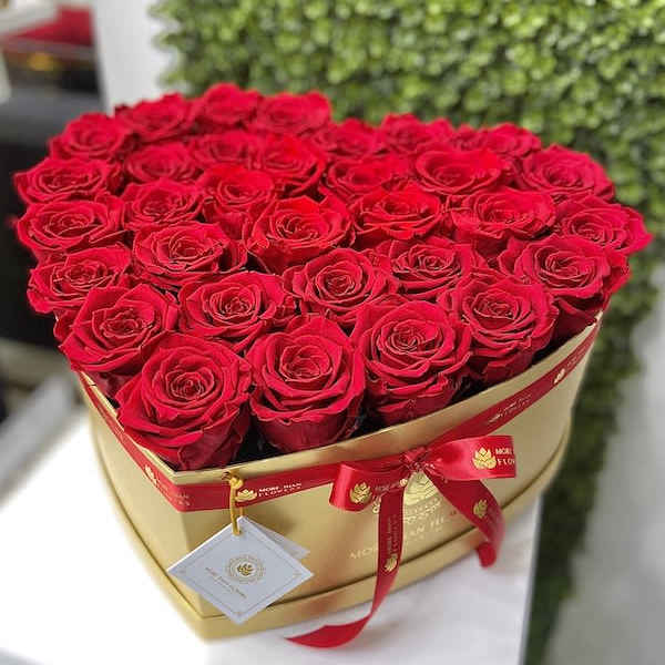 Heart-shaped gold box filled with red roses and tied with a red ribbon and tag