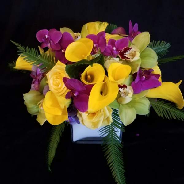 Bouquet of yellow calla lilies, purple orchids, and roses in a white vase