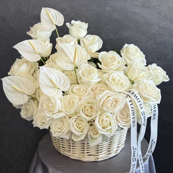 White roses and anthuriums arranged in a wicker basket with ribbon