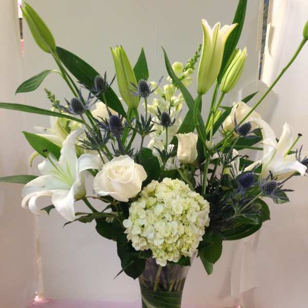 White lilies and roses in a tall glass vase with blue thistle accents