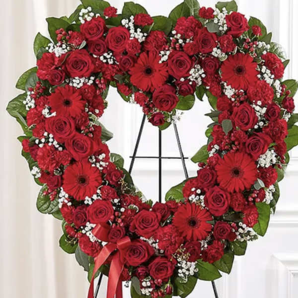Heart-shaped red rose wreath on a stand with a ribbon bow