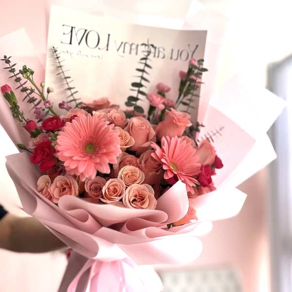 Pink bouquet of roses and gerbera daisies wrapped in pastel paper