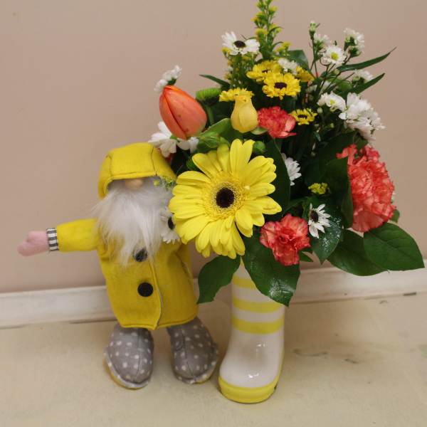 Yellow gerbera bouquet in a striped boot vase beside a small gnome figurine