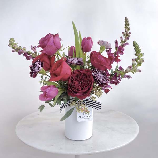 Pink and burgundy bouquet in a white vase with a striped ribbon