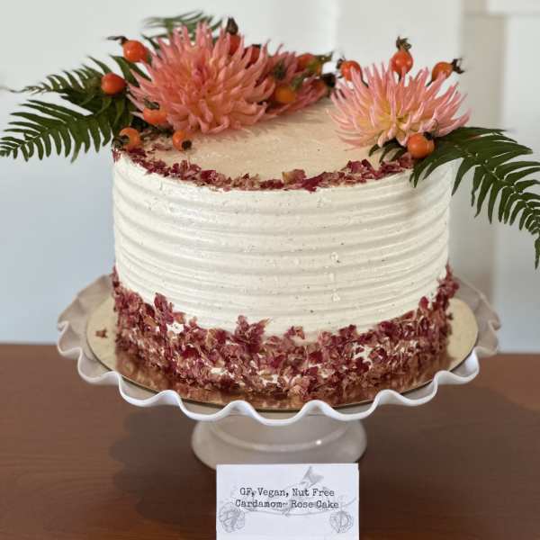 White frosted cake topped with pink flowers and fern fronds
