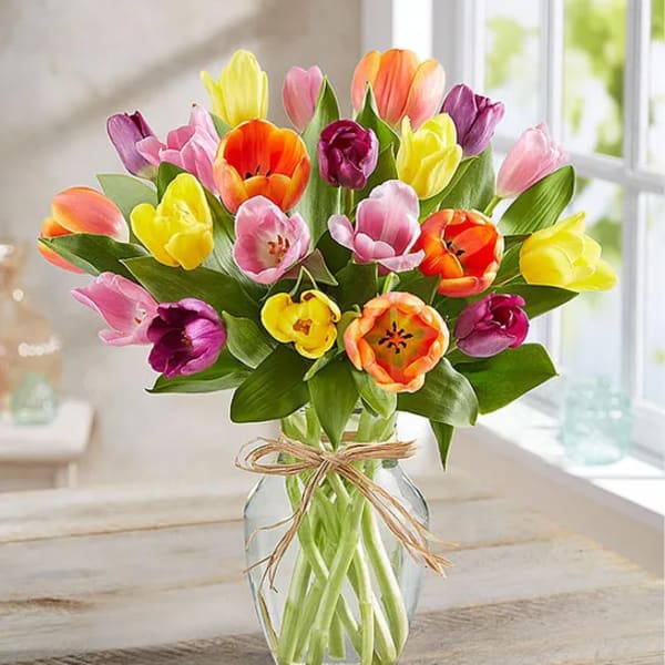 Colorful tulip bouquet in a clear glass vase with a twine bow