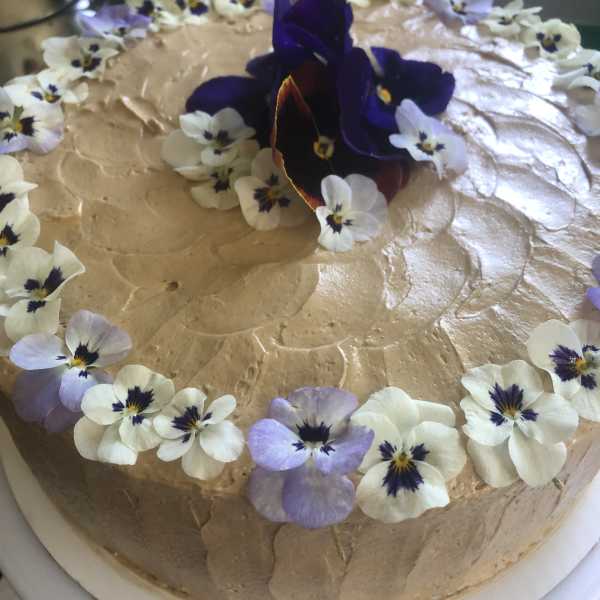 Round frosted cake topped with purple and white edible flowers