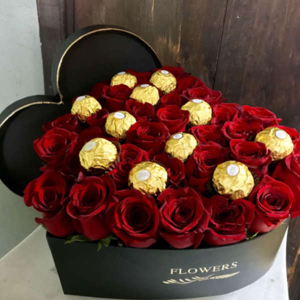 Red roses and gold-wrapped chocolates in a black heart-shaped box