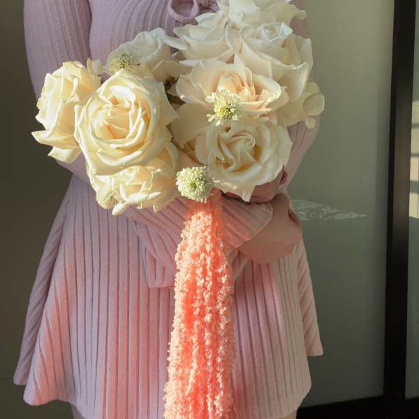 Woman holding a bouquet of cream roses with a peach tassel