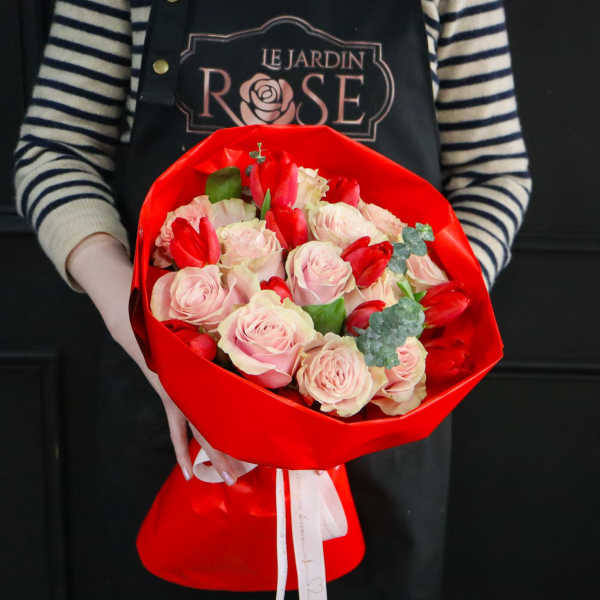 Bouquet of pale pink roses and red tulips wrapped in bright red paper