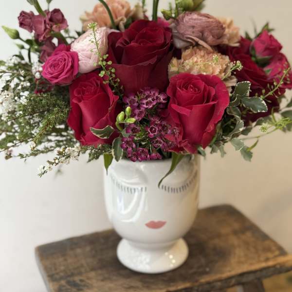 Bouquet of red and pink roses in a white vase with a face design