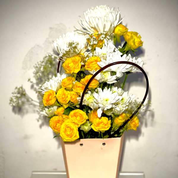 Yellow roses and white daisies in a peach tote-style container