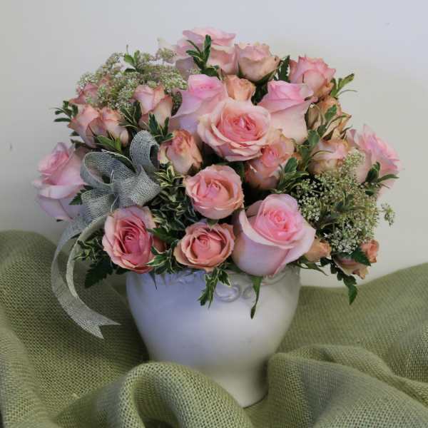 Pink rose bouquet in a white vase with a gray ribbon