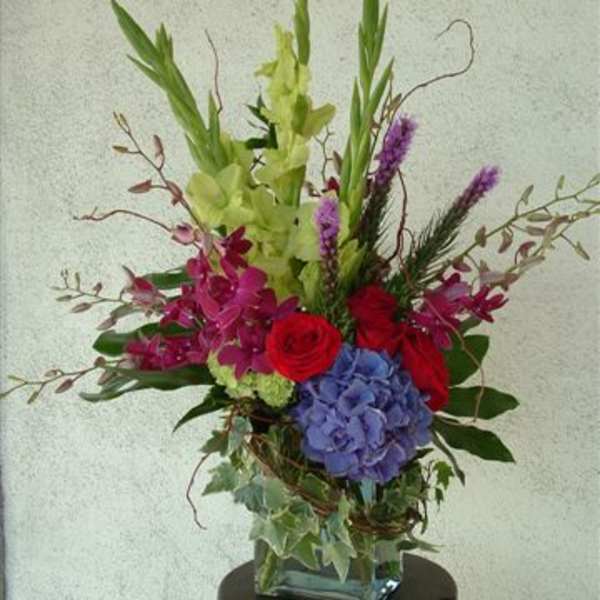Tall mixed floral arrangement in a square glass vase