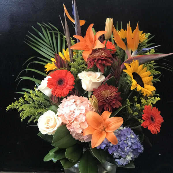 Mixed bouquet with orange lilies, sunflowers, roses, and hydrangea in a glass vase