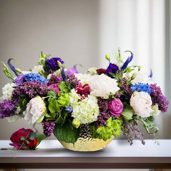 Colorful mixed flower arrangement in a gold bowl with a red rose beside it