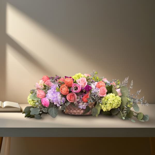 Low floral centerpiece with pink and coral roses in a decorative vase