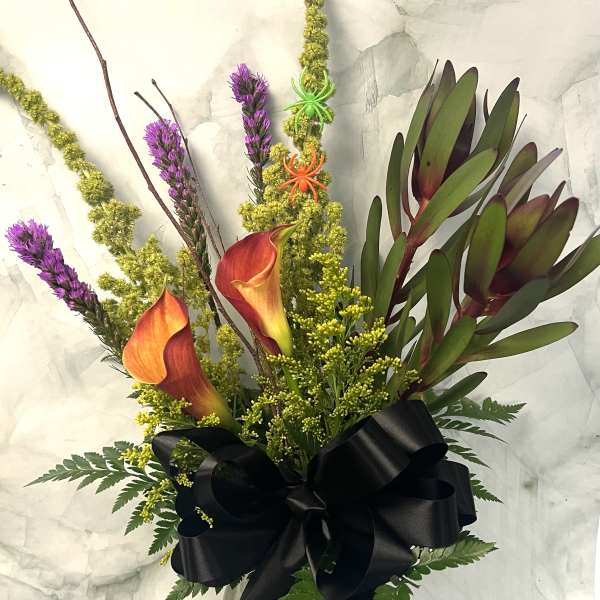 Bouquet of orange calla lilies and purple spikes in a glass vase with a black ribbon