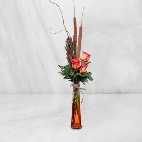 Tall orange rose arrangement in a narrow glass vase with cattails