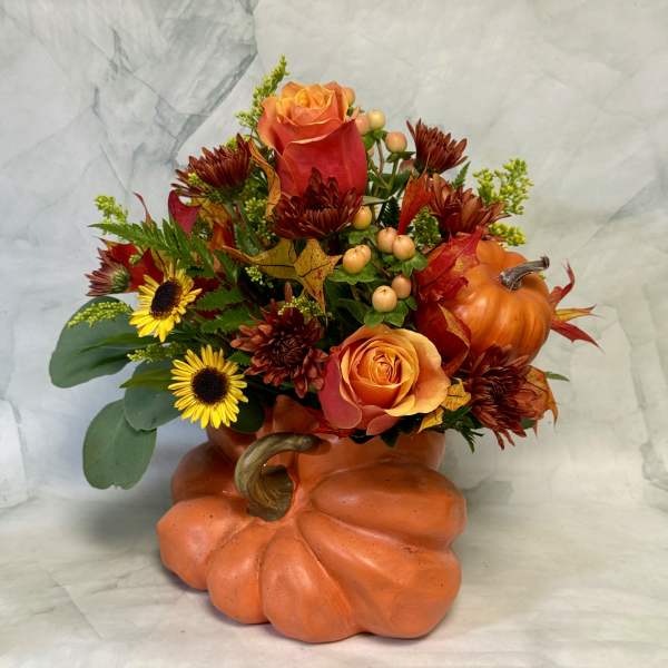 Fall floral arrangement in a pumpkin-shaped container with orange roses and sunflowers
