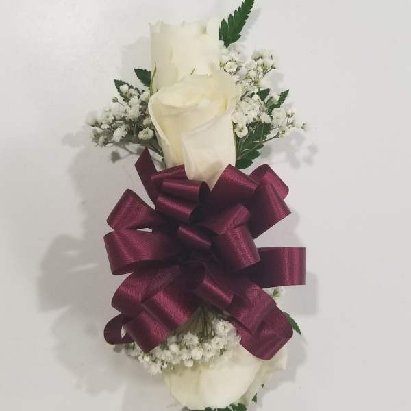 White rose corsage with baby's breath and a burgundy ribbon