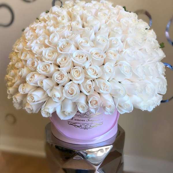 Large dome of white roses arranged in a round pink hatbox-style container on a pedestal