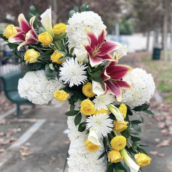 Cross-shaped floral arrangement with white blooms, yellow roses, and burgundy lilies