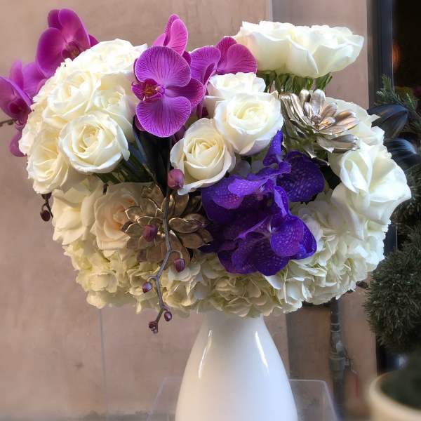 White roses and purple orchids arranged in a white vase