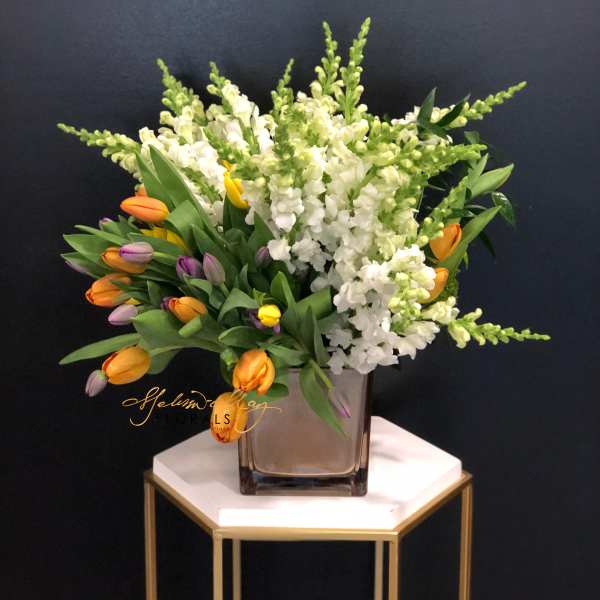 White snapdragons and multicolored tulips in a square glass vase