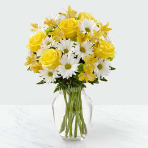 Yellow roses and white daisies in a clear glass vase
