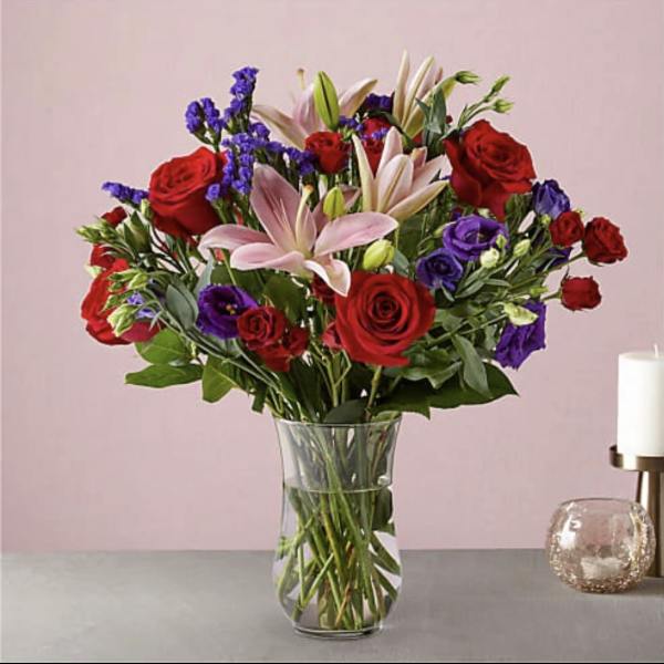 Bouquet of red roses, pink lilies, and purple flowers in a glass vase