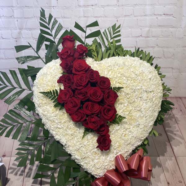 Heart-shaped white floral arrangement with red roses and a pink ribbon bow